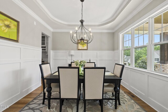 dining room featuring a raised ceiling, a decorative wall, a chandelier, dark wood-style floors, and crown molding