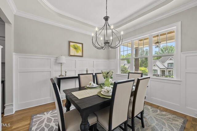 dining area with a decorative wall, crown molding, a tray ceiling, a chandelier, and wood finished floors