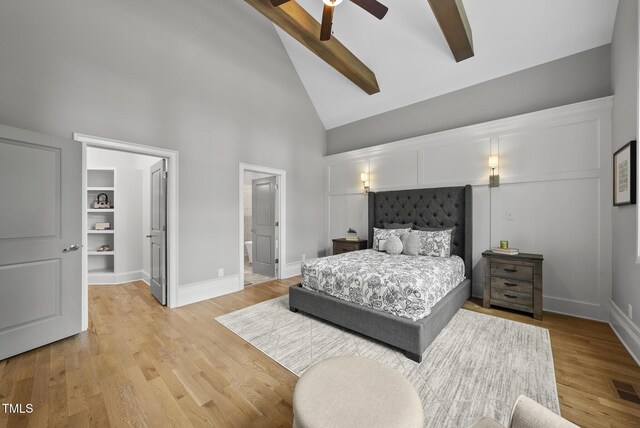 bedroom with high vaulted ceiling, a walk in closet, beamed ceiling, baseboards, and light wood-style flooring