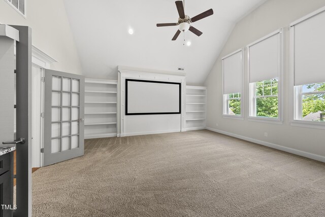 carpeted home theater room with plenty of natural light, ceiling fan, built in shelves, and high vaulted ceiling