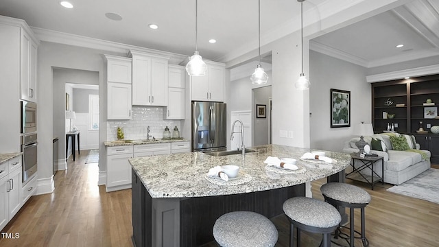 kitchen with stainless steel appliances, wood finished floors, a breakfast bar area, a sink, and white cabinetry