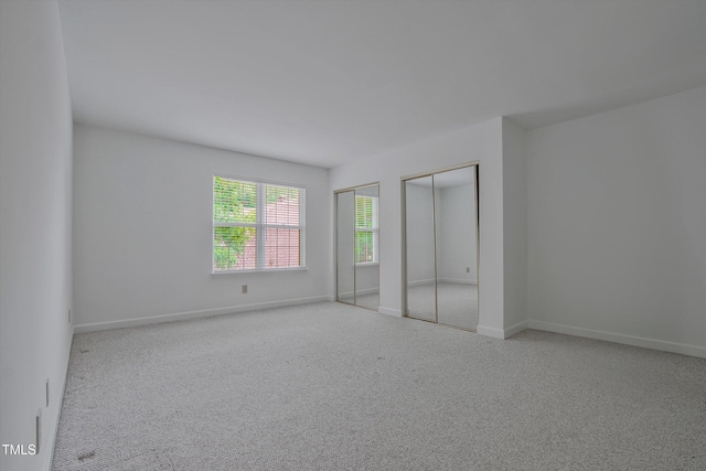 unfurnished bedroom with two closets, carpet, and baseboards