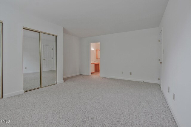 unfurnished bedroom featuring light carpet, baseboards, and ensuite bathroom