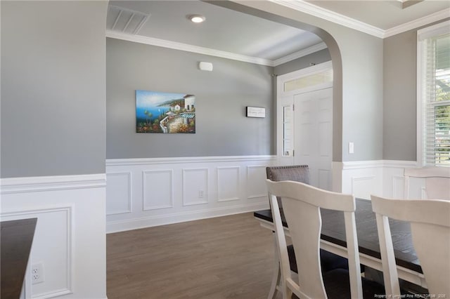 dining space with arched walkways, crown molding, wood finished floors, a wainscoted wall, and a decorative wall
