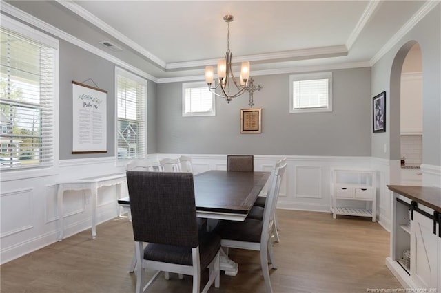 dining area with a decorative wall, a chandelier, arched walkways, ornamental molding, and a tray ceiling