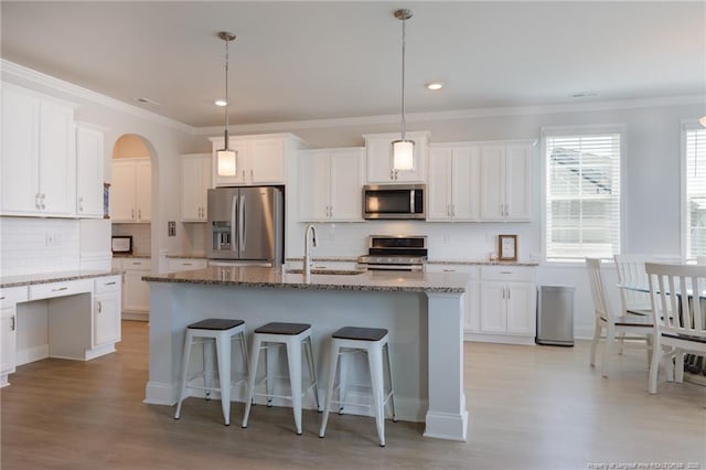 kitchen with appliances with stainless steel finishes, a sink, light wood-style flooring, crown molding, and a kitchen breakfast bar