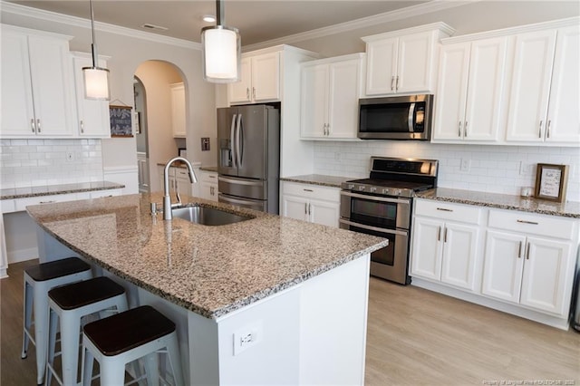 kitchen with appliances with stainless steel finishes, a sink, arched walkways, white cabinets, and crown molding