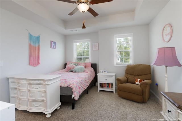 bedroom with a tray ceiling, light colored carpet, and a ceiling fan