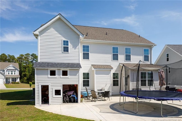 back of house with a trampoline, a patio area, a yard, and a shingled roof