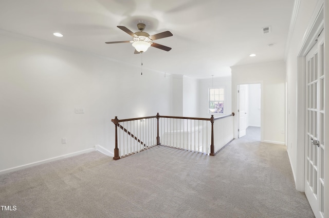 carpeted spare room with visible vents, crown molding, baseboards, and a ceiling fan