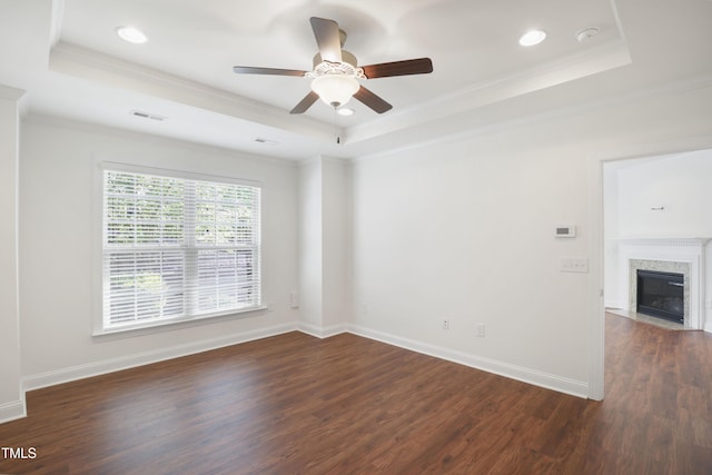 empty room with a tray ceiling, ceiling fan, ornamental molding, and dark wood-style flooring