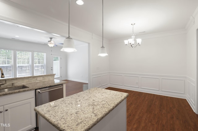 kitchen with light stone counters, a sink, hanging light fixtures, dishwasher, and a wainscoted wall