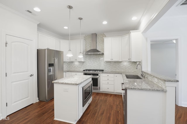 kitchen with wall chimney exhaust hood, stainless steel appliances, a peninsula, a sink, and visible vents