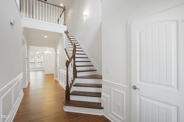 stairway featuring wood finished floors, a decorative wall, wainscoting, and an inviting chandelier
