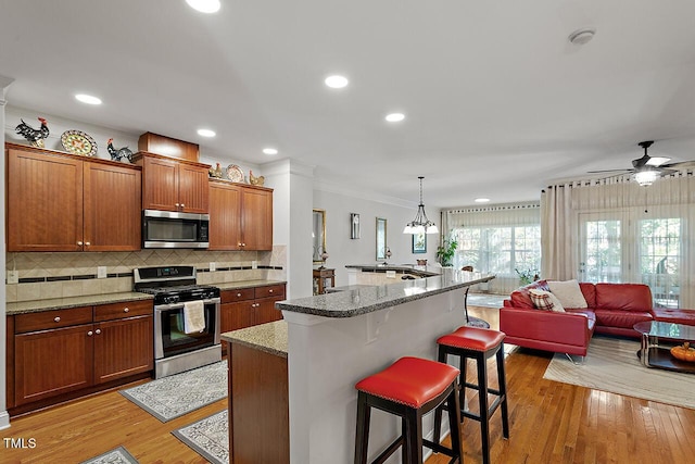 kitchen with decorative backsplash, light wood-style floors, appliances with stainless steel finishes, ornamental molding, and a kitchen bar