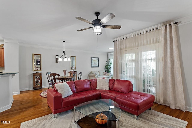 living room featuring crown molding, baseboards, wood finished floors, and ceiling fan with notable chandelier