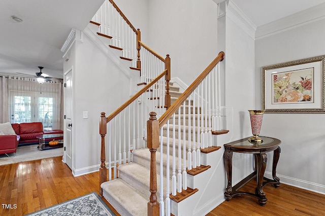 staircase featuring baseboards, wood finished floors, a ceiling fan, and crown molding