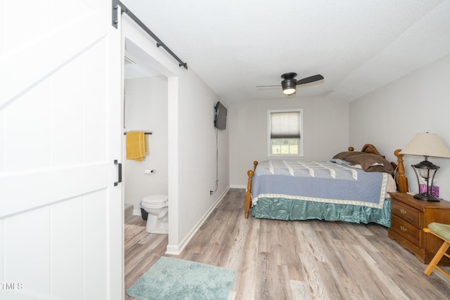 bedroom with a barn door, ceiling fan, light wood-style flooring, baseboards, and ensuite bathroom