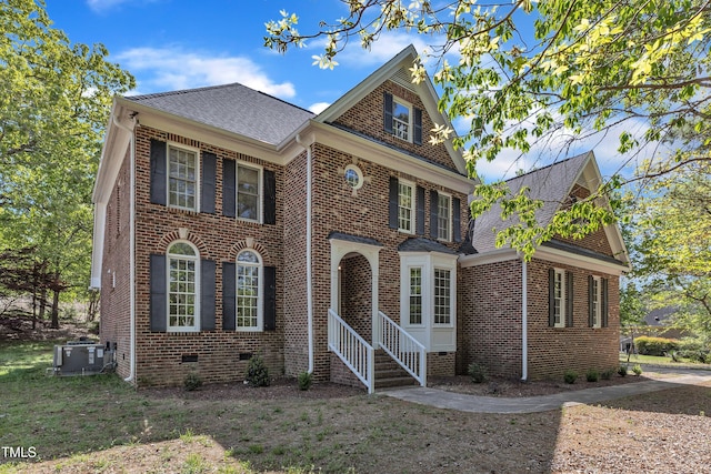 colonial house with roof with shingles, brick siding, and central AC