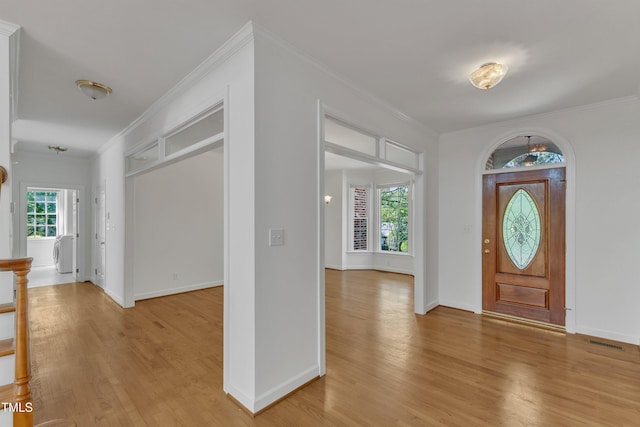 foyer entrance with light wood finished floors, baseboards, visible vents, and crown molding