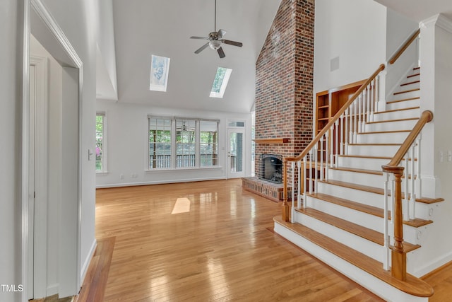 unfurnished living room with stairway, a towering ceiling, a brick fireplace, and ceiling fan