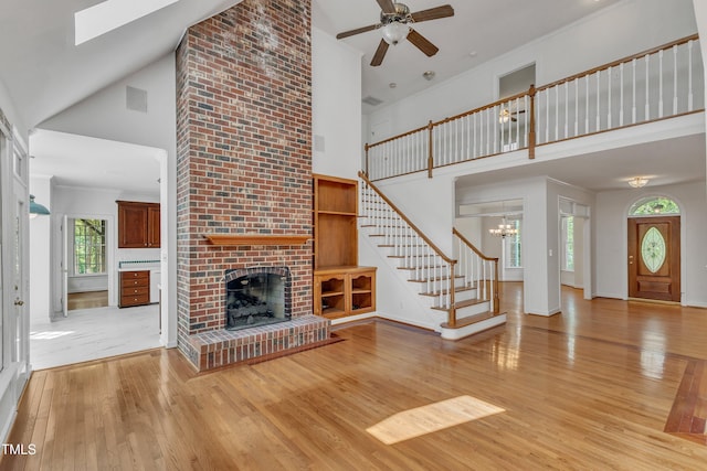 unfurnished living room featuring stairway, wood finished floors, ceiling fan with notable chandelier, a high ceiling, and a brick fireplace
