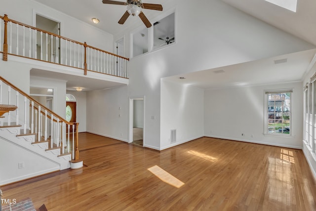 unfurnished living room with stairway, wood finished floors, ceiling fan, a high ceiling, and visible vents