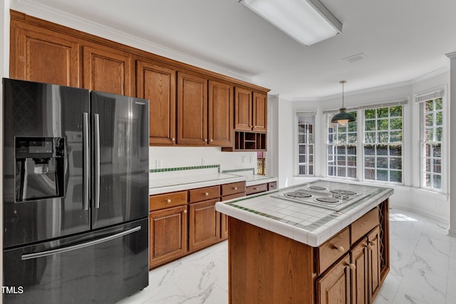 kitchen featuring crown molding, tile counters, brown cabinetry, marble finish floor, and stainless steel fridge with ice dispenser