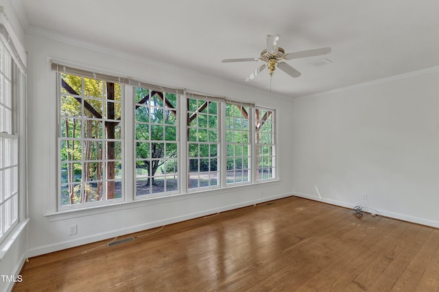 empty room featuring wood finished floors, visible vents, a ceiling fan, ornamental molding, and baseboards