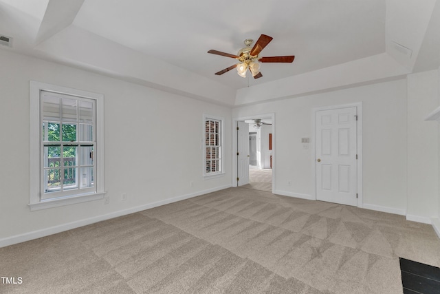 carpeted empty room with baseboards, a ceiling fan, a tray ceiling, and visible vents