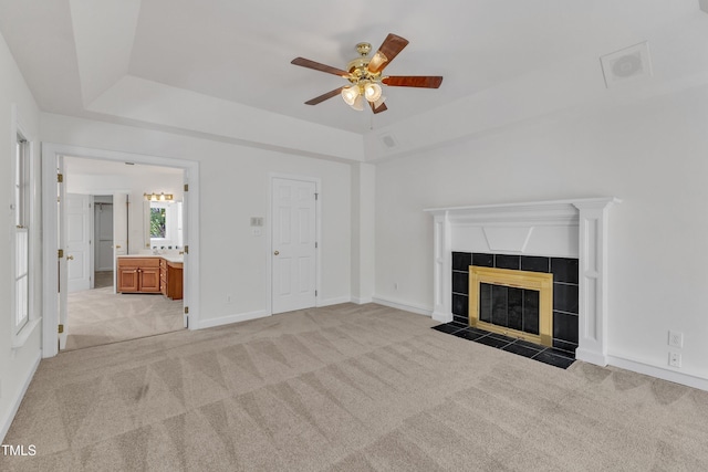 unfurnished living room featuring a raised ceiling, a tiled fireplace, light colored carpet, and ceiling fan