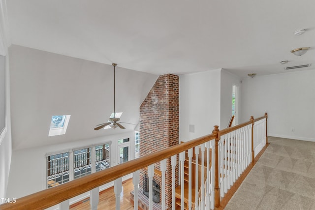 corridor with lofted ceiling with skylight, carpet floors, baseboards, and visible vents