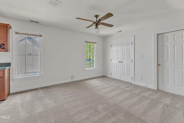 unfurnished bedroom featuring baseboards, light carpet, visible vents, and two closets