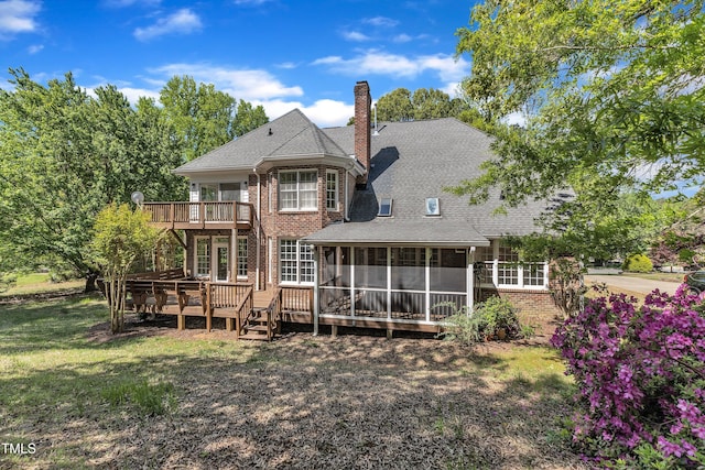 back of house featuring a chimney, a wooden deck, brick siding, a lawn, and a sunroom