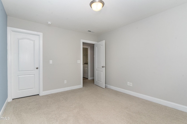 unfurnished bedroom featuring visible vents, baseboards, light colored carpet, and washer / dryer