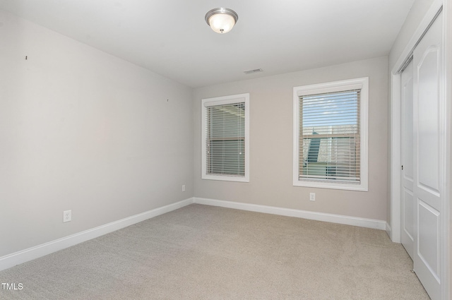 unfurnished bedroom featuring baseboards, light colored carpet, visible vents, and a closet