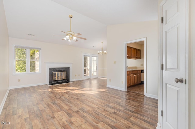 unfurnished living room featuring a wealth of natural light, wood finished floors, ceiling fan with notable chandelier, and lofted ceiling
