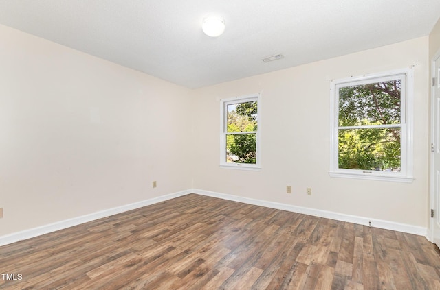 spare room featuring wood finished floors, visible vents, and baseboards