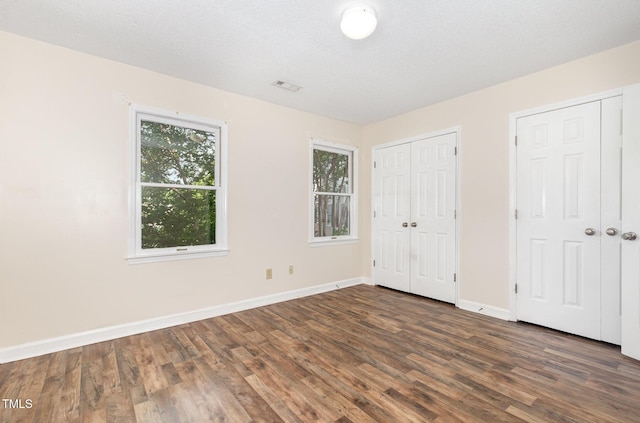 unfurnished bedroom featuring dark wood-type flooring, two closets, baseboards, and multiple windows