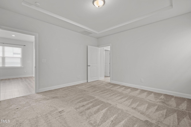 carpeted spare room with crown molding, visible vents, baseboards, and a tray ceiling