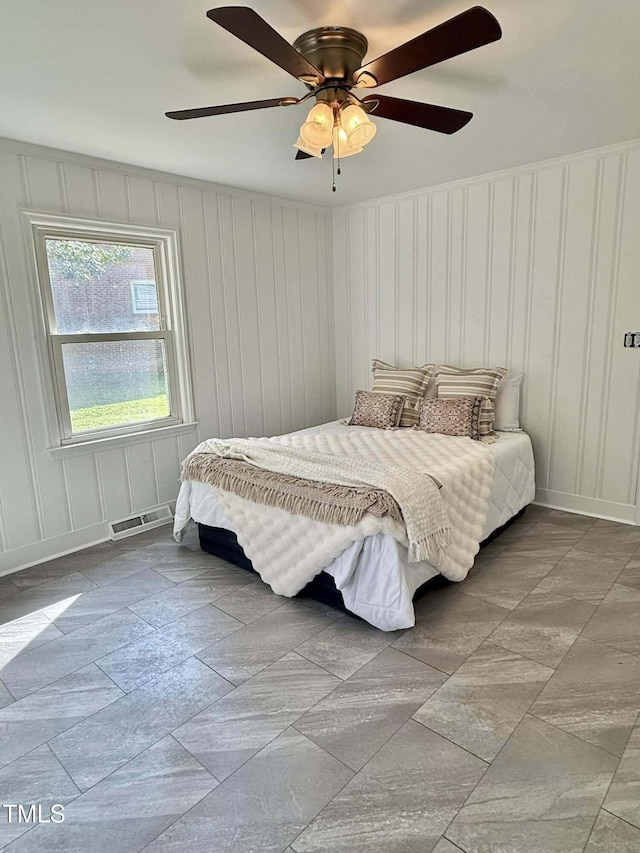 bedroom with a decorative wall, visible vents, and a ceiling fan