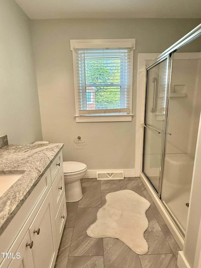 bathroom with toilet, a stall shower, vanity, baseboards, and visible vents