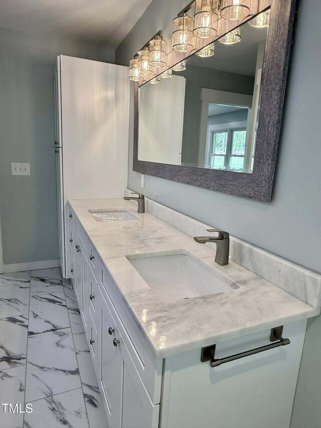 bathroom featuring marble finish floor, baseboards, a sink, and double vanity