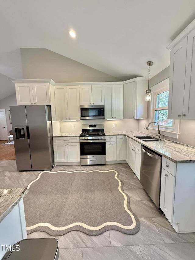 kitchen with lofted ceiling, a sink, pendant lighting, appliances with stainless steel finishes, and white cabinetry