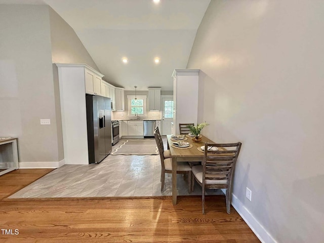 dining room featuring baseboards, light wood-type flooring, and high vaulted ceiling