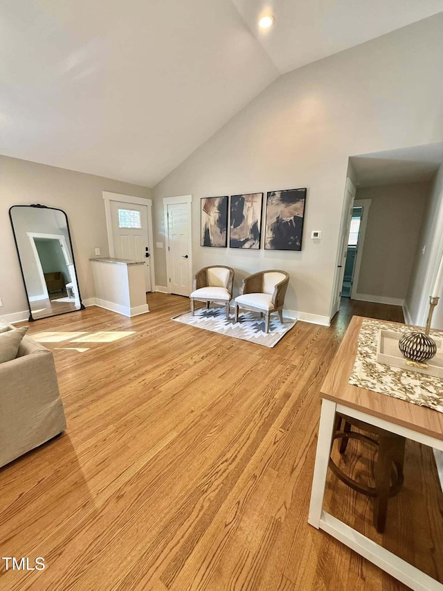 living room featuring lofted ceiling, baseboards, and light wood-type flooring