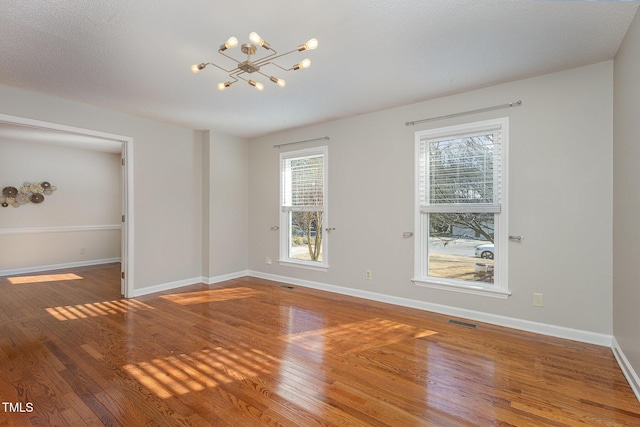 empty room with a chandelier, wood finished floors, baseboards, and visible vents
