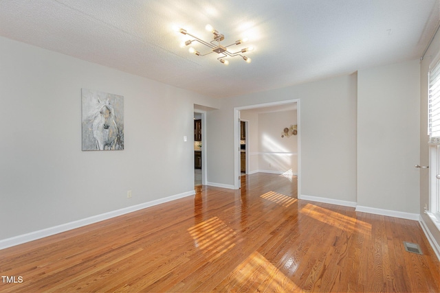 spare room featuring a chandelier, visible vents, light wood-type flooring, and baseboards
