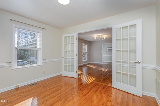 unfurnished room with french doors, wood finished floors, baseboards, and visible vents