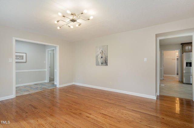 empty room featuring light wood-style floors, a notable chandelier, and baseboards